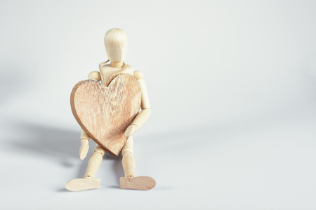 The dummy sits on the board and holding a wooden heart.の写真素材