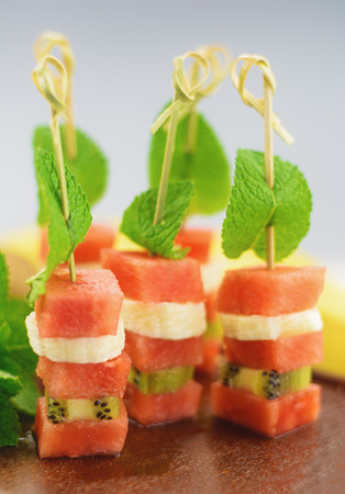 Sandwich of watermelon, kiwi and banana with a mint leaf on a wooden board.の写真素材