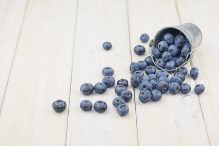 Reversed aluminum bucket with crumbled blueberries on white wooden background.の写真素材