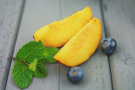 Two slices of peaches, blueberries and a sprig of mint on the table.の写真素材