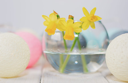 Daffodils in a vase surrounded by round lamps in the form of colored balls on a wooden table.