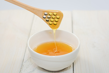 With a honey spoon a bowl is filled with flower honey.の写真素材