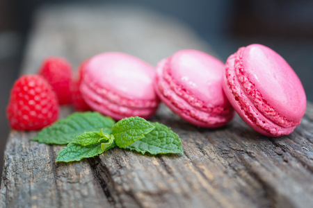 Delicious macarons raspberry flavored with fresh raspberries and a sprig of mint presented on a wooden shelfの写真素材