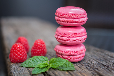 Delicious macarons raspberry flavored with fresh raspberries and a sprig of mint presented on a wooden shelfの写真素材