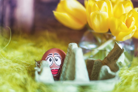 Easter composition with an egg box filled with a egg plastered with a funny face.
