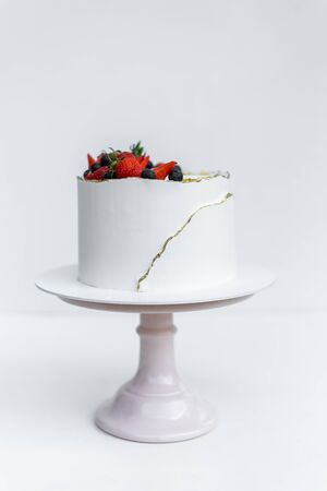 A beautiful white cake with cheese cream, meringues, chocolate and fresh Berries on whiteの写真素材