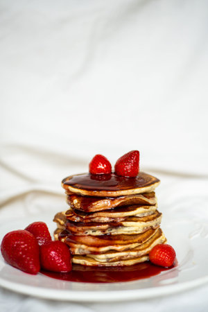 Close-up delicious pancakes, with strawberries and syrup on a light background. Sweet syrup flows...