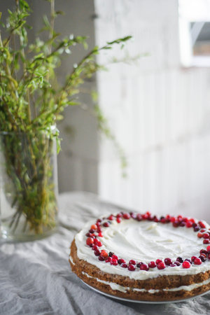 A delicious carrot cake stands on the table, garnished with white mascarpone cream and cranberries....