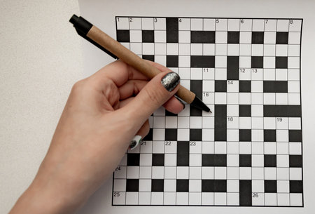 female hand holds a recycled pen in her hands and rejoices a crossword puzzle top view free space