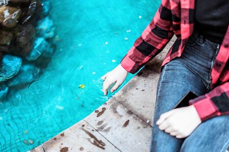 Young girl in red checkered shirt sitting near the fountain.の写真素材