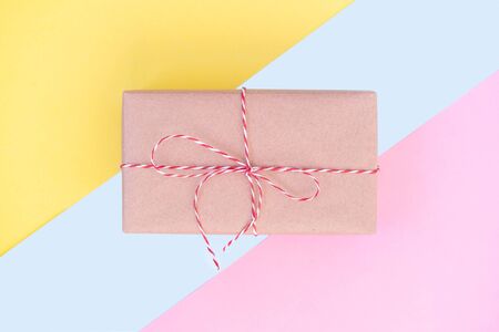 Gift boxe wrapped in craft paper and decorated with red ribbon on colored yellow blue pink background. Valentines day, wedding or other holiday decorations backgroundの写真素材