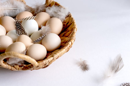White and brown Easter eggs and feathers in a basket on white background. Natural healthy food and...