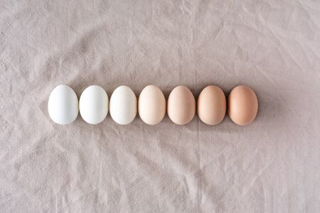 Row of equal chicken eggs on natural linen background. Collection of quail eggs, easter pattern. Flat lay, top view. Easter concept.の写真素材