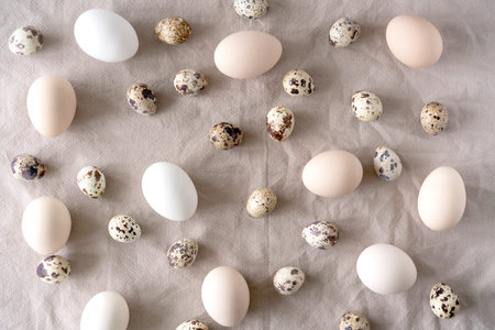 White and brown Easter eggs, quail eggs and feathers on natural linen background. Easter background....
