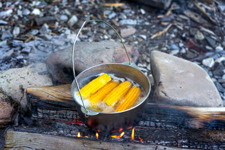 Traveling, tourism, picnic cooking, cooking in a cauldron on the fire, boiling pot with corn at the campfire on picnic.の写真素材