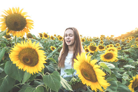 Young beautiful woman smiling and having fun in a sunflower field on a beautiful summer day.の写真素材