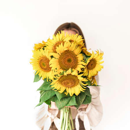 Beautiful young woman in linen dress holding sunflowers bouquet on white background. Autumn concept.の写真素材