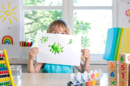 Funny beautiful happy child boy draws laughing with paint. Kid shows drowing of coronavirus. Selective focus.の写真素材