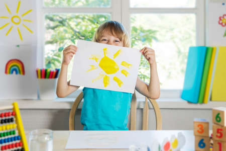 Funny beautiful happy child boy draws laughing with paint. Kid shows drowing of sun. Selective focus.の写真素材