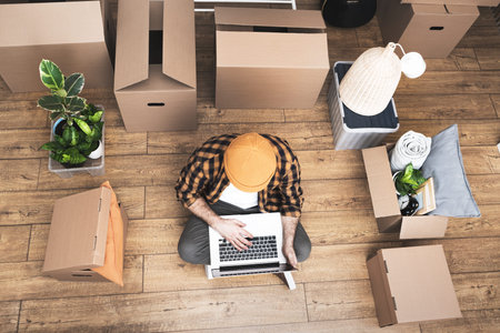 Hipster man with moving boxes in new modern apartment. Happy mature man sitting on the floor of a...
