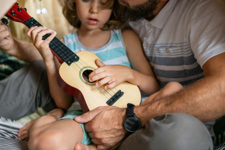 Father and son having fun playing guitar sitting in kid tent at home. Family bonding and enjoying weekend together. Father day.の写真素材