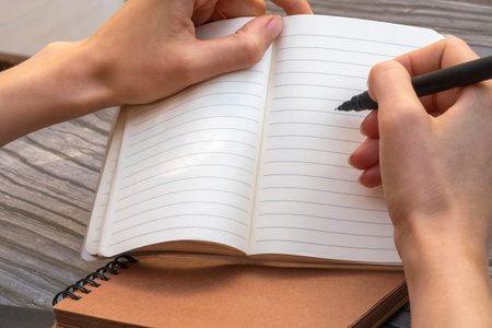 Empty open notebook with lined pages. Woman's hands taking notes with a black liner pen