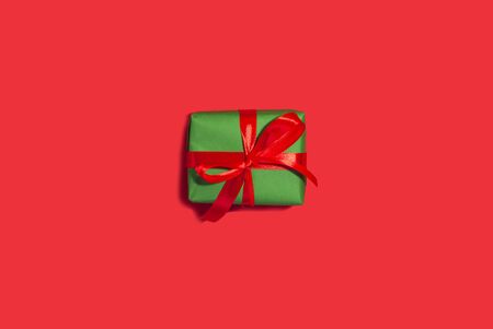 Green New Year gift with ribbon on a red backgroundの写真素材