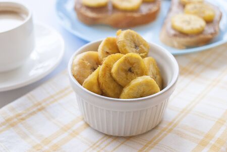 Fried banana, nut paste, white bread, on a white plate. A cup of coffee with milk. Conception of breakfastの写真素材