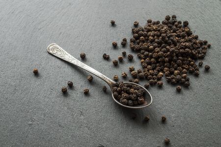 Black pepper peas on a dark background of stone, a silver spoon. Close-up .の写真素材