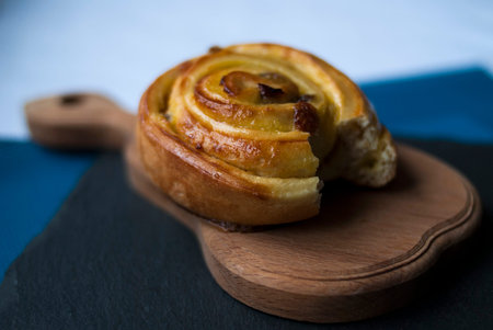 Bitten bun curl with cream and raisins on a dark board, close-up