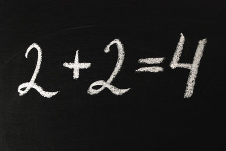 Word two plus two equals four written in white chalk on a black chalkboard.