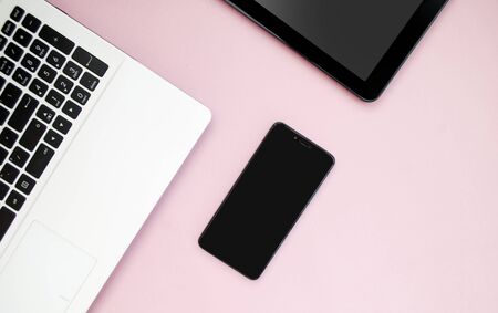 Black-white laptop keyboard, black tablet, black mobile phone on a pink background. Copy space. Top view. Computer work. Flat layの写真素材