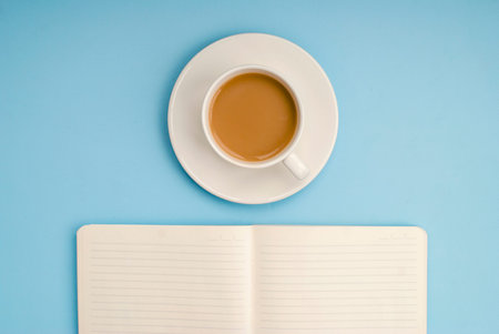 White open notebook for notes, a white cup of coffee with milk on a blue background, place for text