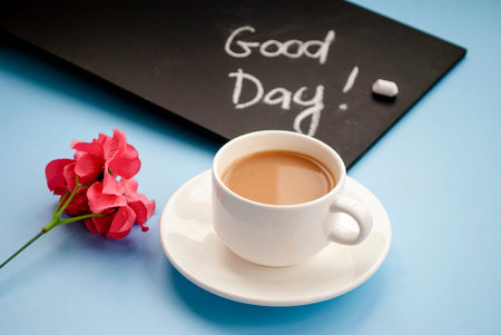 Conception good morning. Black chalk board with the inscription good day, a cup of pink coffee coffe on a light blue background. Flat lay