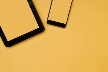 Black tablet and black phone on an orange background. Place for text. Top view. Flat layの写真素材