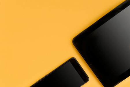 Black tablet and black phone on an orange background. Place for text. Top view. Flat layの写真素材