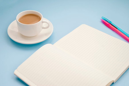 White cup of coffee silver notepad, pink flower on a blue background. Flat lay. copy space.