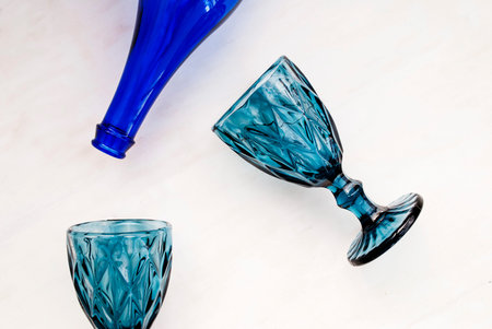 Two blue faceted glasses for wine, a blue bottle on a white background. Top view. Flat lay