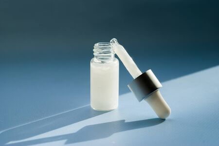 Cosmetic oil, transparent bottle with a dropper, blue background. Place for text. Skin care. Hard shadowの写真素材
