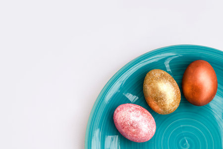 Three multi-colored shiny Easter eggs on a blue plate. White background. Place for text