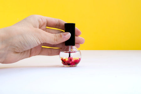 Nail care, cuticle oil in the hand, in a beautiful bottle on a yellow background. Place for text