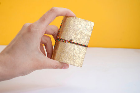 A small notebook in a hand, in a gold cover, on a yellow background. Place for text