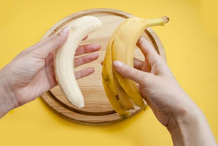 Peel a banana with his hands on a yellow background.の写真素材