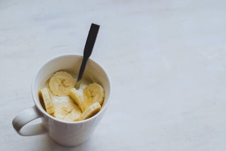 White yogurt with banana in a white cup on a light background.の写真素材