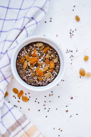 Homemade chocolate with dried apricots, raisins, flax seeds, sesame seeds. White dish light background. Top viewの写真素材