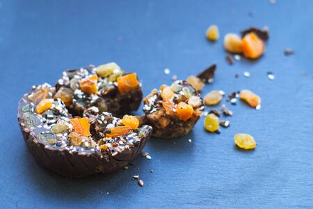 Sliced ââhomemade chocolate with dried apricots, raisins, flax seeds, sesame seeds. on a blue background.の写真素材