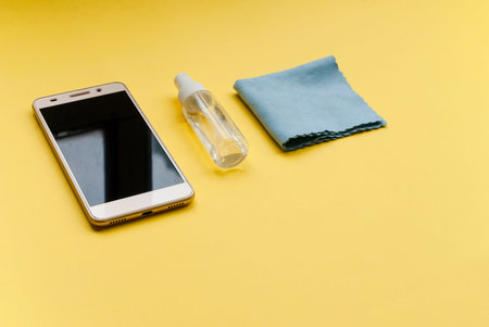 Mobile phone and antiseptic agent on a yellow background, place for text