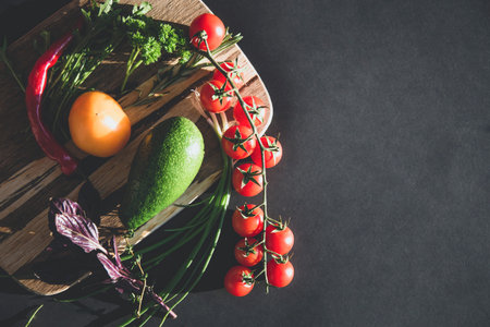 Different fresh raw vegetables on the wooden chopping board. Tomatoes, avocado, basil, arugula, parsley. Healthy cooking and Vegan or diet food concept. Background layout with free text space.の写真素材