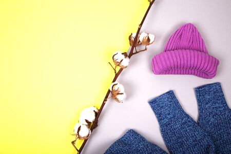 Winter knitted hat, sweater and cotton branch on a yellow and grey paper background, minimalism, top view, flat lay style. Fashion winter compositionの写真素材
