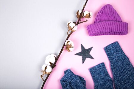 Winter knitted hat, sweater, star and cotton branch on a colored paper background, minimalism, top view, flat lay style. Fashion winter compositionの写真素材